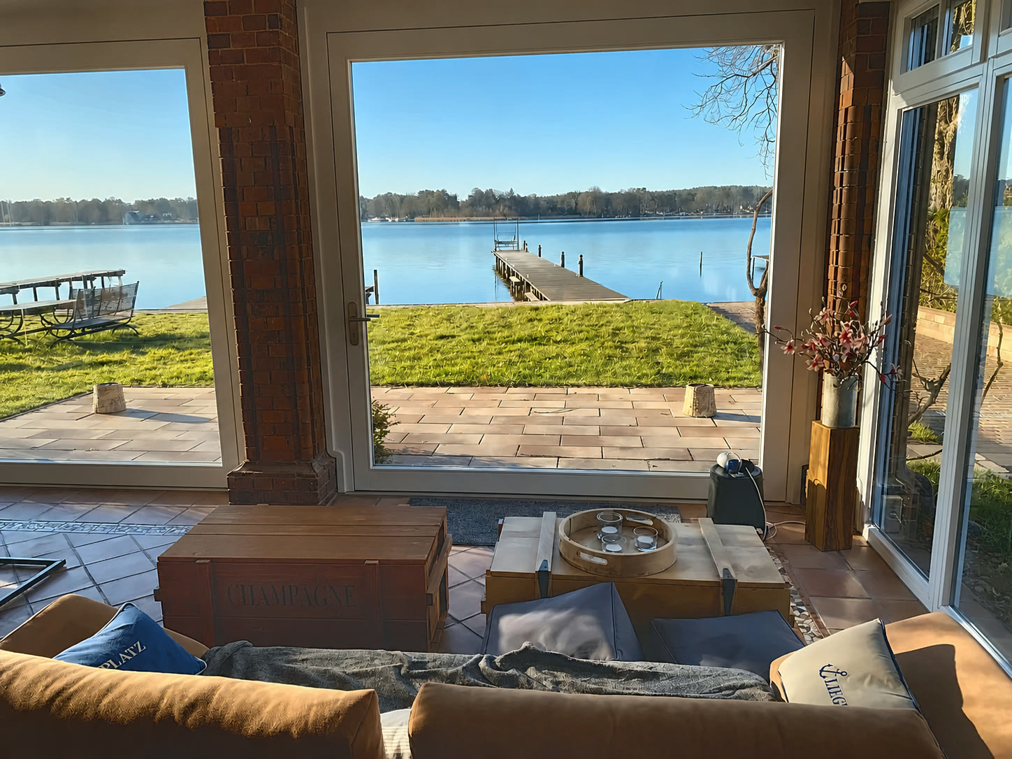 Wohnbereich mit bodentiefem Panoramafenster zum Krüpelsee – Sitzgruppe mit Blick auf Terrasse, Uferwiese und Steg