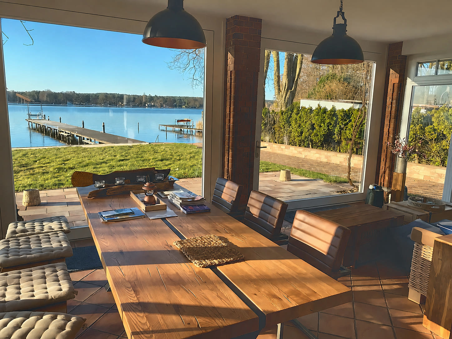 Wintergarten mit massivem Esstisch und Lederstühlen, Blick über die Uferwiese auf den Steg am Krüpelsee