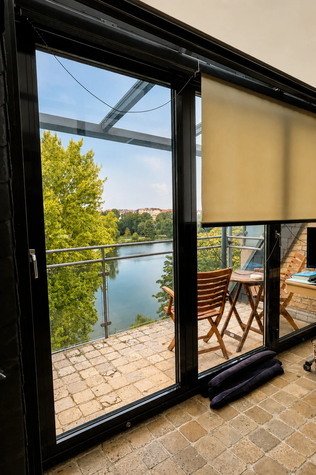 Blick durch die Fensterelemente auf die Terrasse mit Holzmöbeln und Seeblick